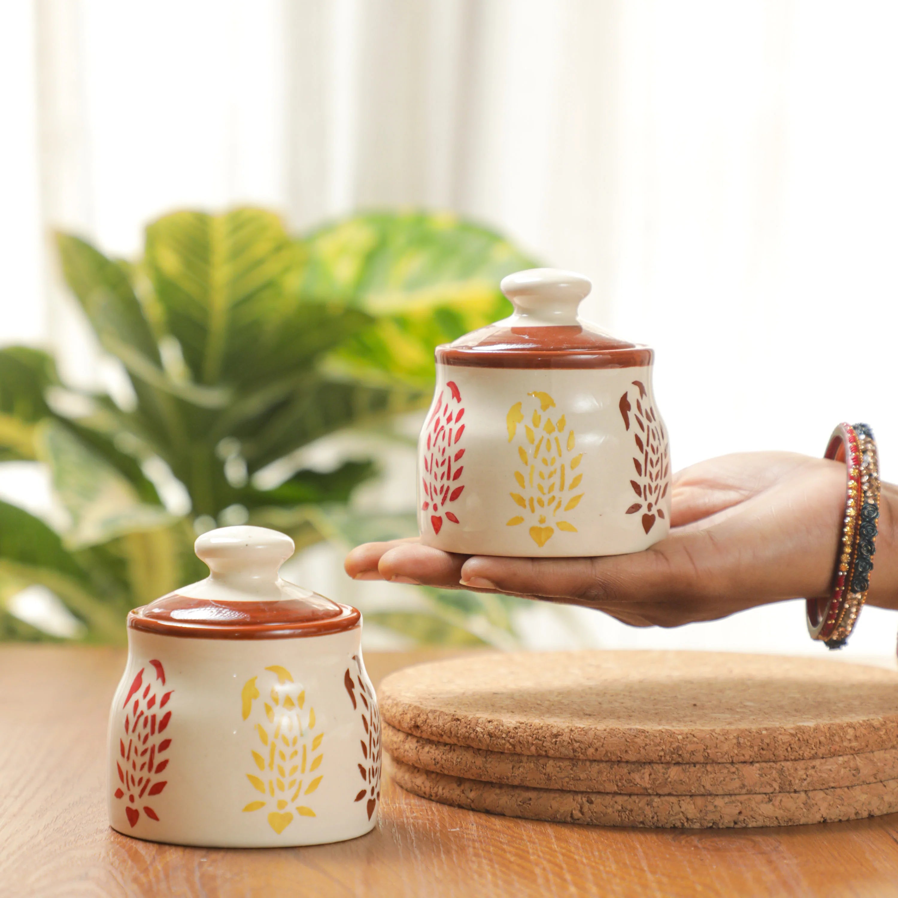 Two ceramic jars with floral designs on a wooden surface with a blurred plant background