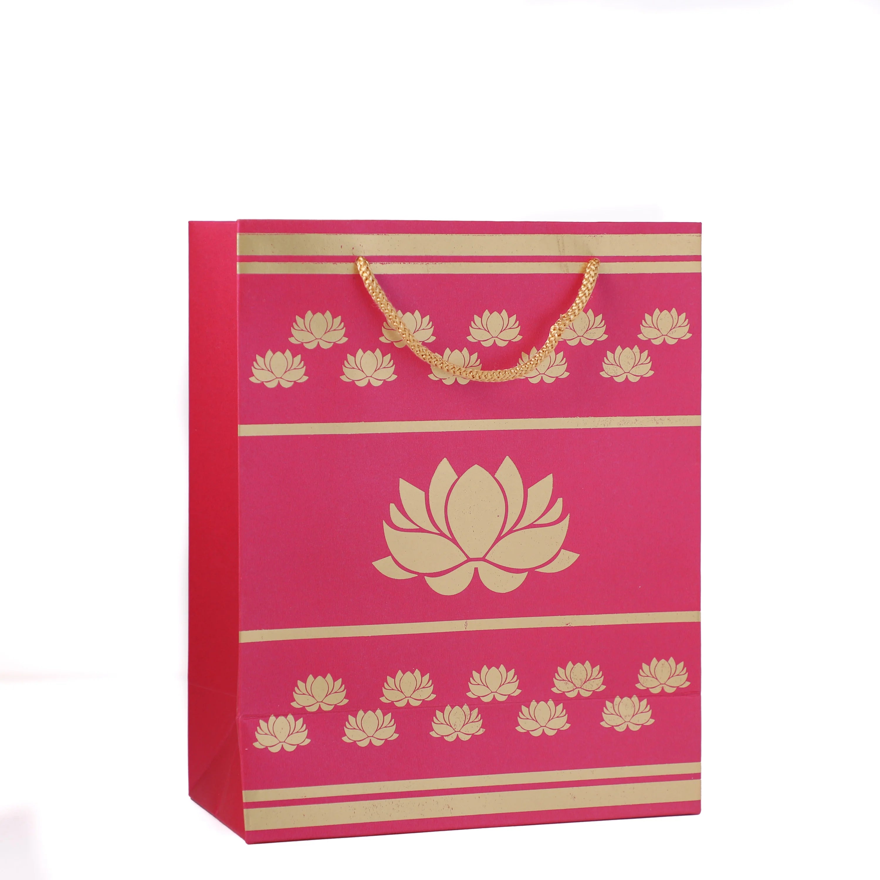 A bright pink gift bag with gold printed lotus flower motifs, horizontal gold stripes, and a gold chain handle, shown on a plain white background.