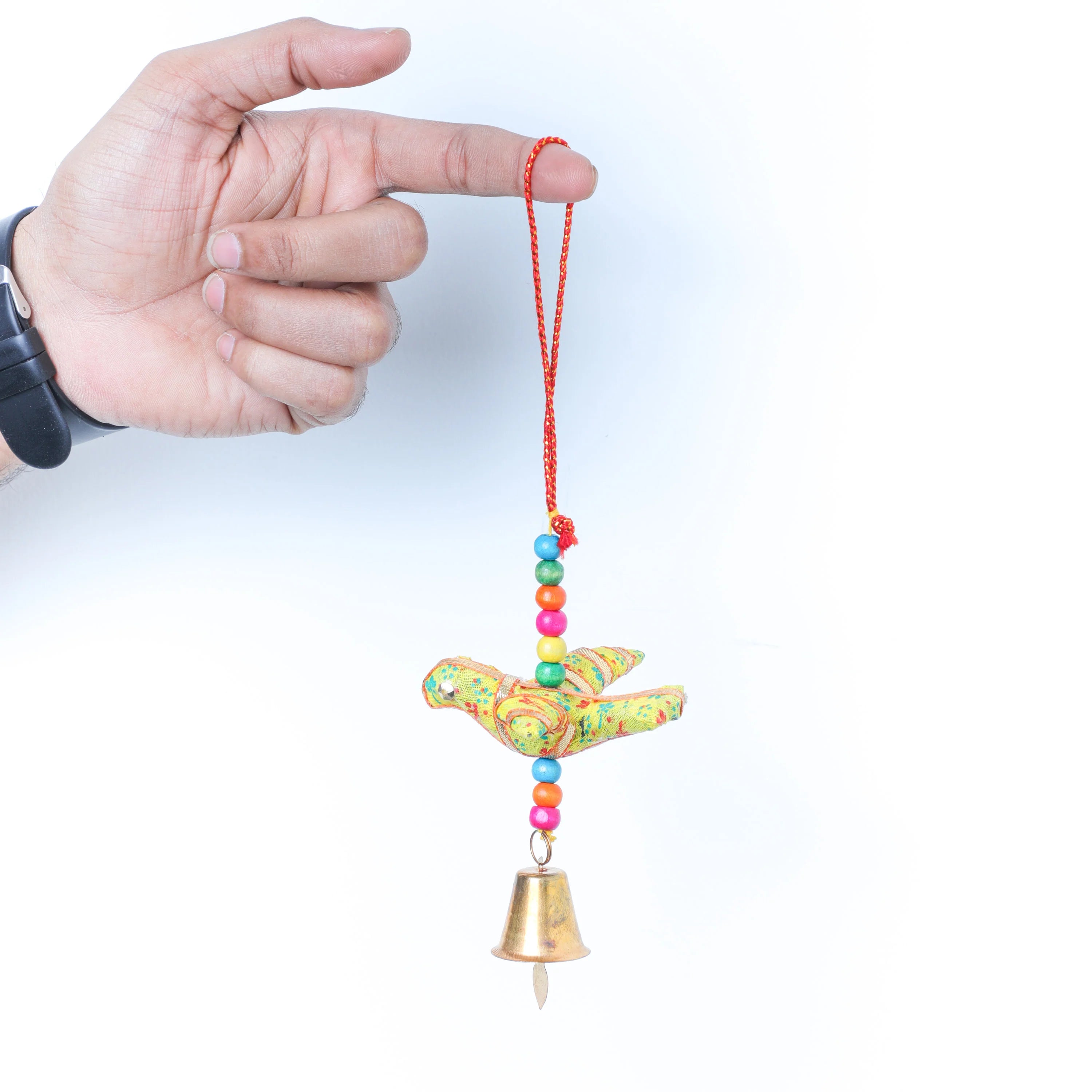 A hand holding a small hanging ornament against a plain white background. The ornament features a colorful patterned bird with a red hanging cord, multicolored beads, and a small gold bell at the bottom.