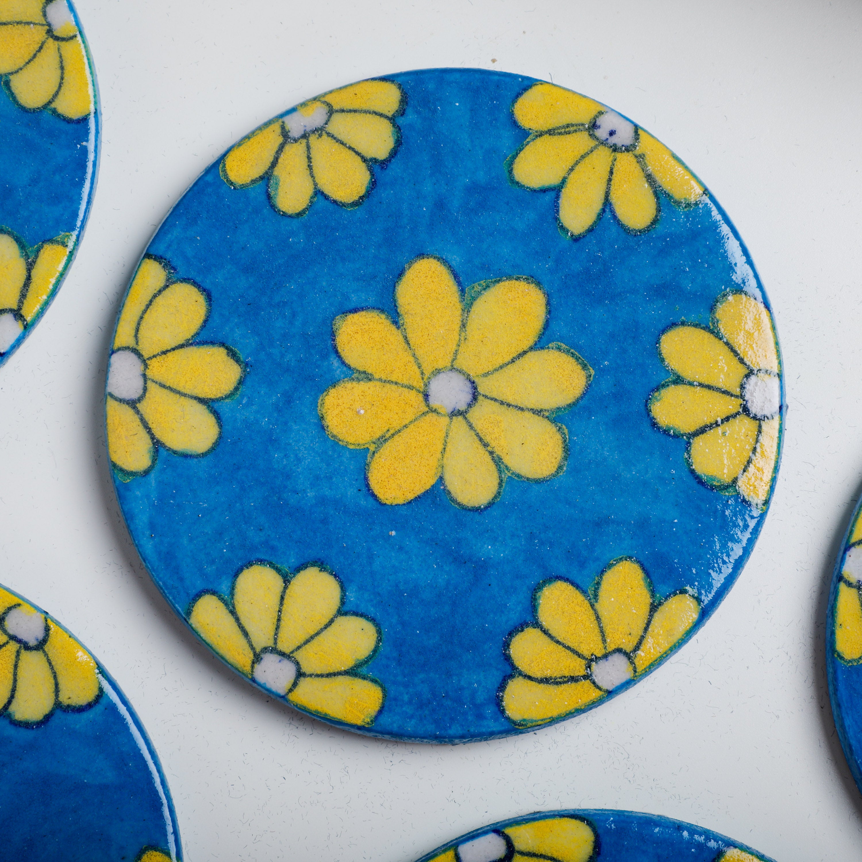 decorative ceramic coaster features a white base, topped with flowers painted with yellow colors