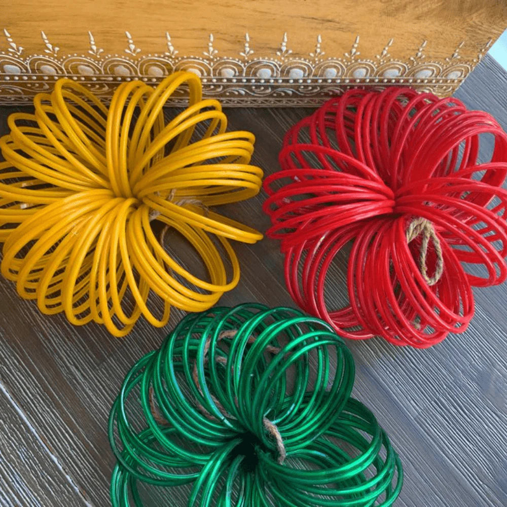 Three coiled decorative pom-pom ornaments in yellow, red, and green, arranged on a dark wood surface with a patterned wooden box in the background.